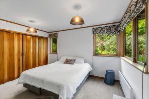 a bedroom with a bed and two windows at Treetop Sanctuary - Titirangi Holiday Home in Auckland