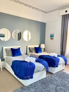 two beds in a bedroom with blue pillows and mirrors at Bishopton Apartment, near Glasgow in Bishopton