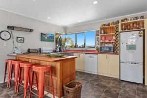 a kitchen with a counter with stools and a refrigerator at The Bachela - Ohope Beach Holiday Home in Ohope Beach