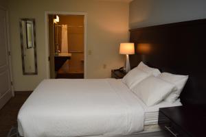 Staybridge Suites Syracuse Liverpool, an IHG Hotel في ليفربول: غرفة نوم بسرير كبير عليها شراشف ووسائد بيضاء