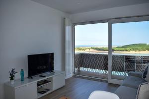 uma sala de estar com um sofá, uma televisão e uma varanda em Apartamentos Playa de Mogro em Miengo