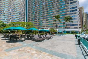 a patio with chairs and umbrellas in front of a large building at Ilikai Tower 1137 Yacht Harbor View 1BR in Honolulu