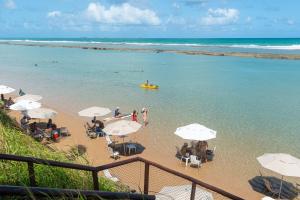 ein Strand mit Stühlen und Sonnenschirmen und Menschen im Wasser in der Unterkunft Nannai Residence Muro Alto Porto de Galinhas por Brevelar in Porto De Galinhas