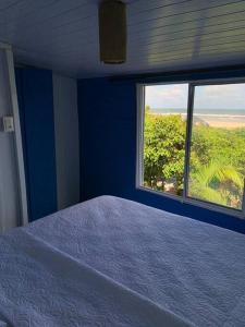Dormitorio azul con cama y ventana en Bela Vista - Casa Beira Mar en Paranaguá