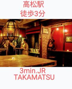 two people in a room with a table and a guitar at Takamatsu Guesthouse BJ Station in Takamatsu