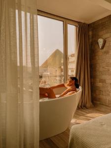 uma mulher sentada numa banheira num quarto com uma janela em Sphinx golden gate pyramids view no Cairo