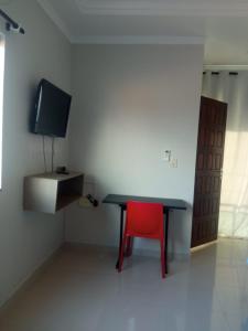 a room with a table and a red chair and a tv at House Suites in Paragominas