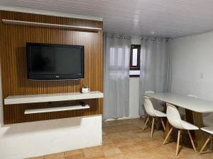 sala de estar con mesa y TV en la pared en BS01- Casa Aconchegante| Equipada| Churrasqueira|, en Balneário Barra do Sul