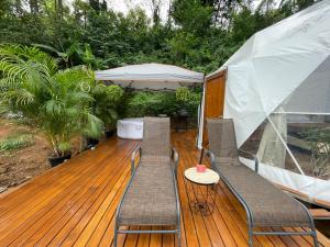 eine Holzterrasse mit 2 Stühlen und einem Sonnenschirm in der Unterkunft La Comarca River Glamping Dome near Manuel Antonio in Manuel Antonio