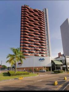 a tall building with a palm tree in front of it at Flat Manaus Hotéis Millenniun in Manaus