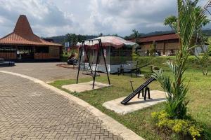 un parque infantil con columpio y sombrilla en Capital O 93437 Embung Banteran Cottage, en Banyumas