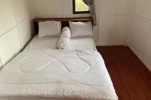 Cama en habitación pequeña con sábanas y almohadas blancas en Capital O 93437 Embung Banteran Cottage, en Banyumas