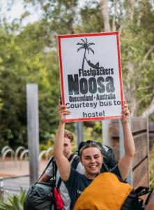Un uomo che tiene un cartello con una palma di Noosa Flashpackers a Sunshine Beach