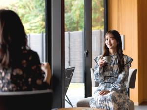 Kumano-bettei Nakanoshima في كاتسورا: امرأة جالسة على كرسي عقد كوب من القهوة