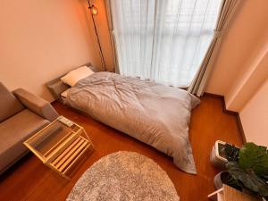 Bett in einem Zimmer mit Sofa und Fenster in der Unterkunft 東横のヨコ in Okayama