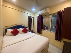 a bedroom with a bed with red pillows and a window at Hotel Royal Grand - Near Mumbai International Airport in Mumbai
