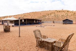 a beach with chairs and a building in the desert at Sand Delight Camp in Al Wāşil
