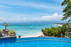 a swimming pool in front of a beach with boats in the water at Lembongan Island Beach Villas in Nusa Lembongan