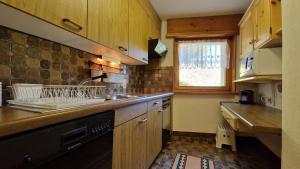 a kitchen with wooden cabinets and a black dishwasher at Chesa Bellaval, Haus la Vuolp 2,5-Zimmerwohnung in Silvaplana