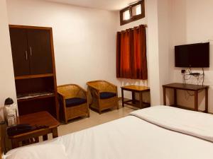 a bedroom with a bed and chairs and a tv at Hotel Devika in Dibrugarh