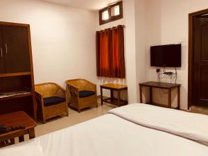 a bedroom with a bed and a tv and chairs at Hotel Devika in Dibrugarh