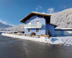 a blue house in the snow next to a road at Ferienwohnung Astl in Kirchdorf in Tirol