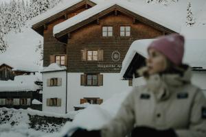 a girl sitting in the snow in front of a house at Margarethe Apartments Lech in Lech am Arlberg