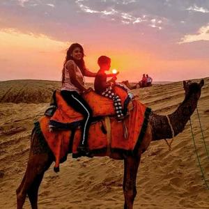 a woman and a child riding a camel in the desert at Jaisal heritage desert camp in Jaisalmer
