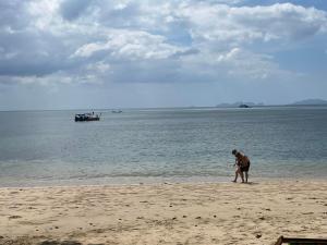 Un uomo in piedi sulla spiaggia con una barca in acqua di Kohjum Relax Beach a Koh Jum