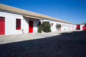 a white building with red doors and a driveway at CORTIJO RURAL LA MARISCALA in Jerez de la Frontera