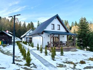 une maison blanche avec un toit noir dans la neige dans l'établissement Domki Potok - Noclegi Bieszczady, à Stefkowa