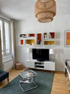 a living room with a television on a white table at Appartement à côté de la plage avec balcon filant in Trouville-sur-Mer