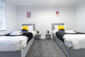 two beds in a room with white walls and yellow pillows at Kirkview Apartment in Kirk of Shotts
