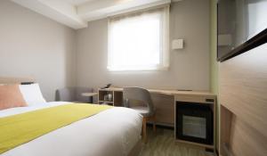 a bedroom with a bed and a desk and a window at Nest Hotel Hakata Station in Fukuoka