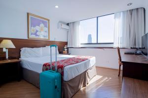 a hotel room with a bed with a blue suitcase at Hotel Dan Inn Curitiba Centro By Nacional Inn in Curitiba