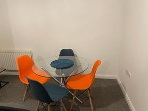 três cadeiras e uma mesa de vidro com cadeiras laranja em Jdb Romford Apt - Cosy 2 Bedroom with parking em Harold Wood