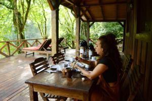 a woman sitting at a wooden table on a deck at Margay - Reserva Natural y Lodge de Selva in El Soberbio