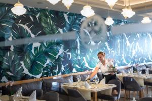 a man standing at a table in a restaurant with a mural at Tsokkos Protaras Beach Hotel in Protaras