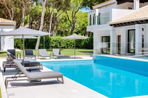 a pool with lounge chairs and umbrellas next to a house at Pine Cliffs Village in Albufeira