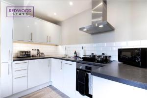 una cocina con armarios blancos y encimeras negras en 2 Bedroom 1 Bathroom Town Center Apartment With FREE Parking By REDWOOD STAYS, en Basingstoke