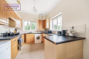 a kitchen with wooden cabinets and a black counter top at 2 Bedroom Apartment, Business & Contractors, FREE Parking & Netflix By REDWOOD STAYS in Basingstoke
