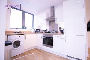 a kitchen with white cabinets and a washer and dryer at Festival Place, Modern Town Center Apartment, Perfect for Contractors & Families, FREE Parking & WiFi by REDWOOD STAYS in Basingstoke