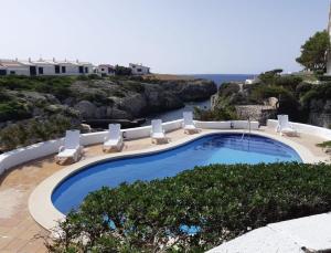 a swimming pool with chairs and the ocean in the background at Apartamentos Islanders in Cala en Forcat