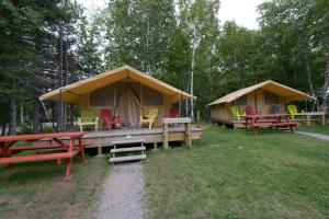 a group of tents with tables and chairs in the grass at Prêts-à-camper Camping Tadoussac in Tadoussac