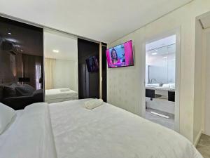 a bedroom with a white bed and a tv on the wall at Sofisticado APT ao lado do Paraguai 3 quartos in Foz do Iguaçu