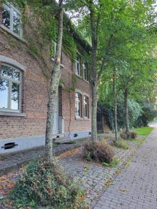 um edifício de tijolos com árvores em frente em Charming and cosy ART DECO house in old historic farm with private natural pool and gardens with hiking and cycling trails nearby em Sint-Truiden