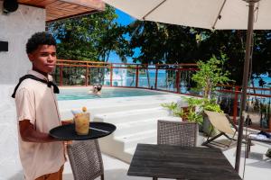 a man holding a drink on a table next to a swimming pool at AL MAR SUÍTES in Praia do Forte