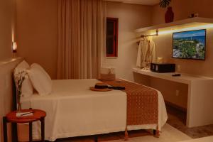 a bedroom with a white bed and a table and a window at AL MAR SUÍTES in Praia do Forte