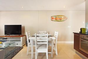 a white dining room with a table and a tv at Eden on The Bay 125 by HostAgents in Bloubergstrand