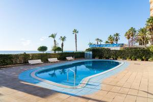 una piscina con bancos y el océano en el fondo en Hauzify I Apartament Llevant en Santa Susanna